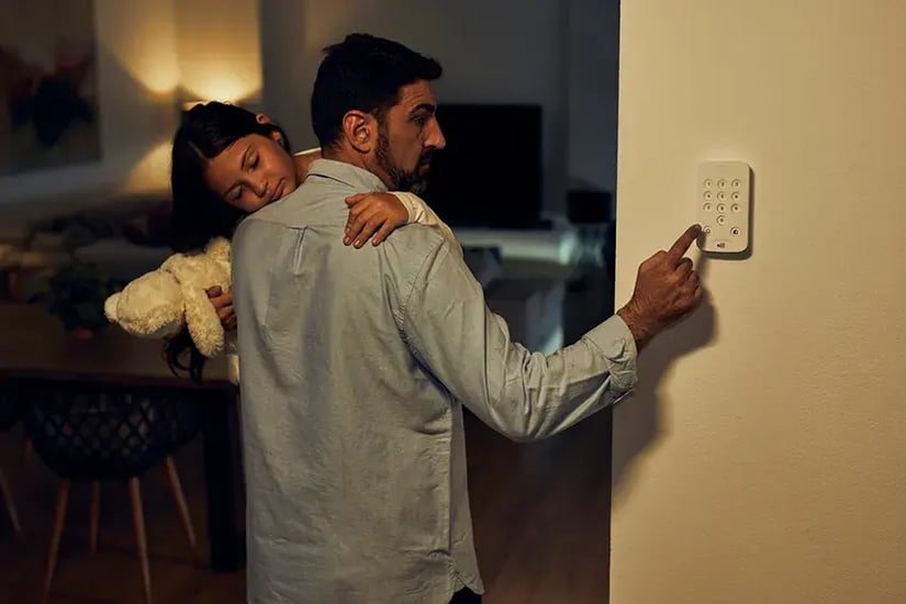 Person entering home security alarm code while carrying a child holding a teddy bear at night