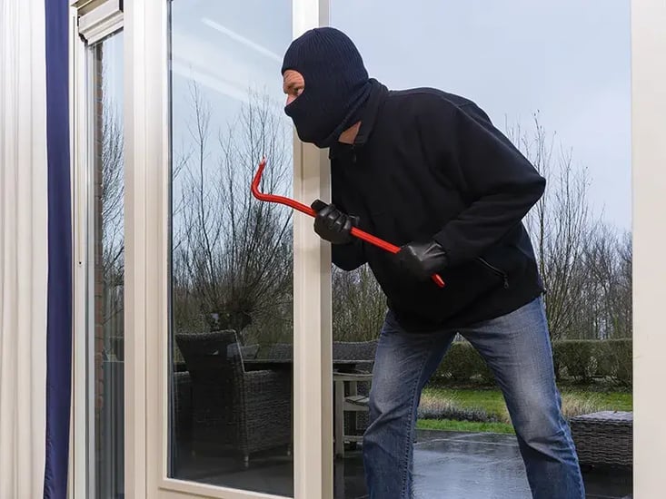Masked intruder attempting to force entry through a patio door using a crowbar