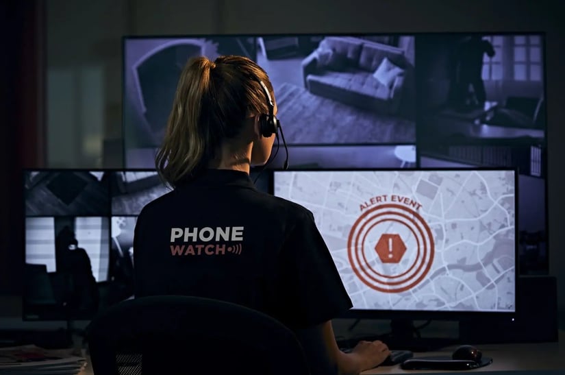 PhoneWatch security monitoring operator at desk with multiple screens showing alert event and home surveillance feeds
