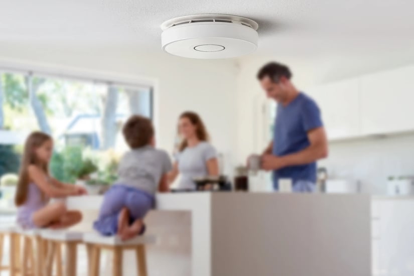 photo of smoke detector with young family in kitchen in the background