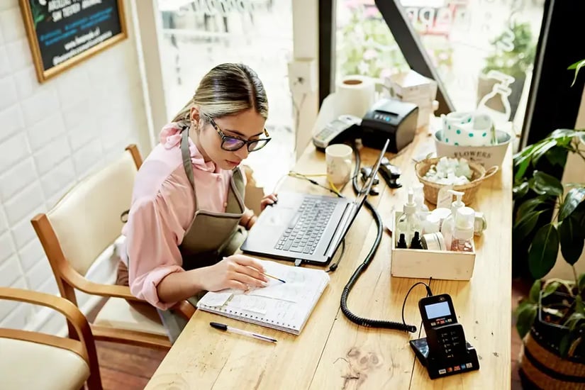 Small business owner managing accounts and orders from a laptop at a retail shop counter